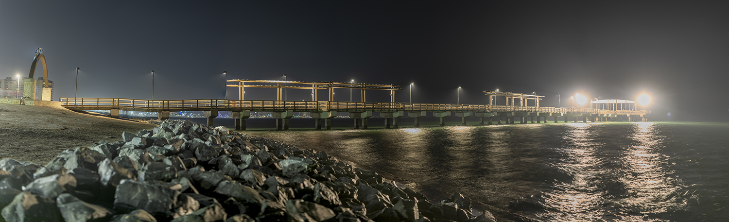 The illuminated Lawrence Street T-Head fishing pier and the Mirador de la Flor monument along the Corpus Christi Bayfront at night.